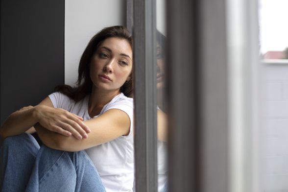 Mujer joven asomada a la ventana con expresión ausente, representando como ayudar a una persona con bloqueo emocional.